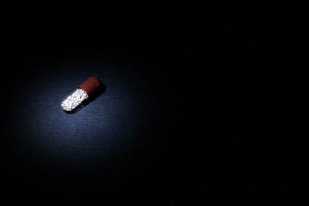 Single pill capsule with contents in light area amongst darkness on a black  backgroundの写真素材