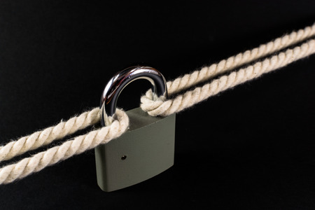 Locked padlock secures two separate ropes together under tensionの写真素材
