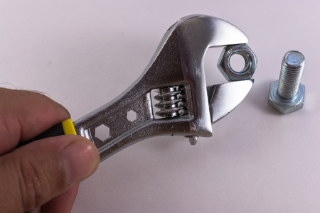 Human hand holding an adjustable spanner and fixing a nut to a bolt on a white backgroundの写真素材