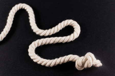 Loose white rope with a single knot at the end on a black backgroundの写真素材