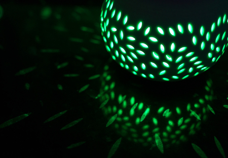 Green lantern at night creates many light patterns on a black reflective surface