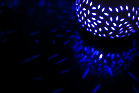 Blue household lantern at night creates many light patterns on a black reflective surfaceの写真素材