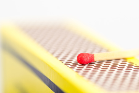 Studio macro close up of a red match head about to strike the honeycomb shaped rough striking surface of a matchboxの写真素材
