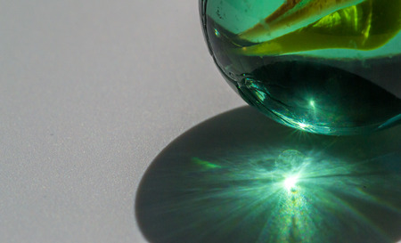 Strong sunlight shines through a glass marble creating an abstract light pattern on a white backgroundの写真素材