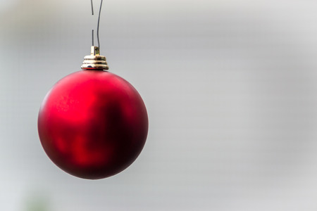 Single red christmas bauble hanging against a grey empty background with no people
