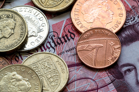 Assorted English Coins of varying values lay on top of a British Fifty pound note with the queens head partially visible from underneathの写真素材