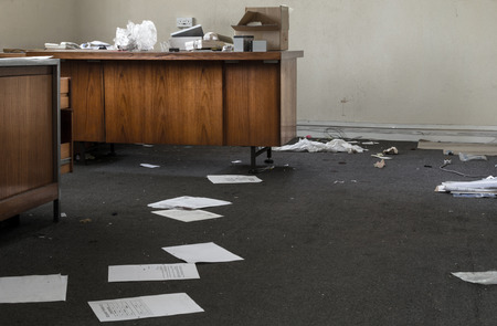 Abandoned Office with strewn discarded papers and rubbish on old wooden desksの写真素材