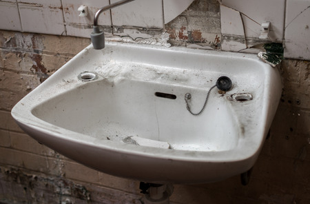 Broken and vandalized industrial factory bathroom sink with ripped piping and cracked tiling and missing tapsの写真素材