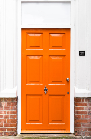 Single bright orange painted wooden door with red brickwork and white walls