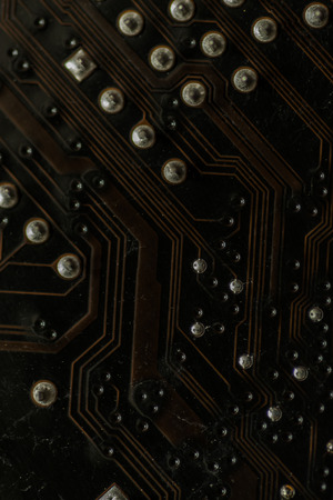 Macro closeup of a computer PCB Motherboard using brown and black colors with silver soldered terminalsの写真素材