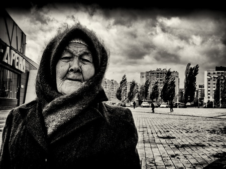 09/10/2015 - An elderly woman wearing a home-knitted woollen shawl and hat with scarf stands up strongly as a fierce wind blows behind her. Men and trees in the background struggle against the howling wind, while the old woman is unaffected in Sterlitamakのeditorial素材
