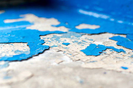 Close-up Macro of flaking blue paint on a white concrete background. The painted surface is in a...