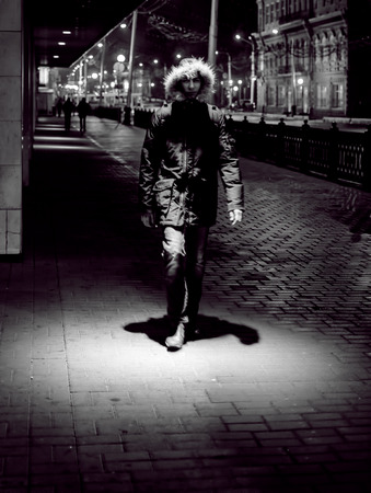 17/10 - Single hooded man walking on a illuminated city street during a rain storm in Ufa, Russia in...