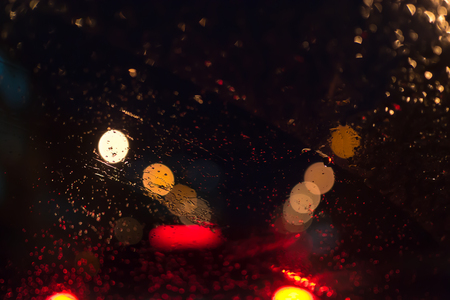 Defocused car lights in a city center with rainwater reflections on the windscreens at night
