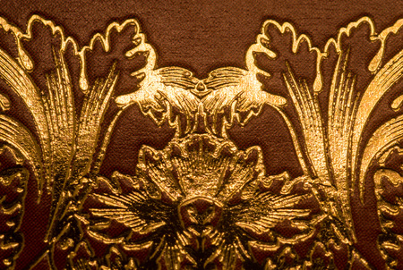 Ornate golden gilding swirls on a brown paper or leather materialの写真素材