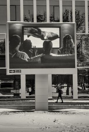 02/11 - Young woman wlaks under an outdoor television  displaying a hapy family watching a television in Ufa, Russiaのeditorial素材