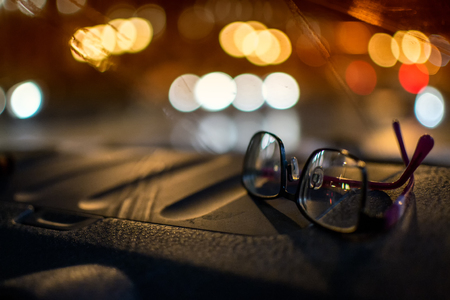 Pair of women driving glasses sitting on a car dashboard at night with defocused car headlights in the backgroundの写真素材