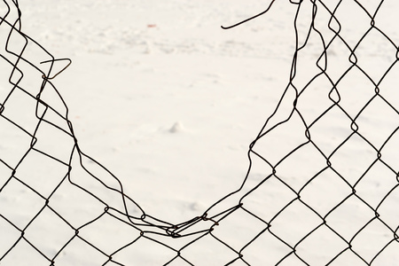 Broken chain link fencing with a white winter snow backgroundの写真素材