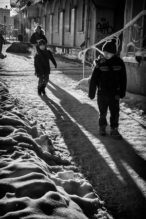 UFA - RUSSIA 19TH DECEMBER 2015 - Two children walk along a winter sunlit path covered in snow, as one boy waits for his friend to play or jump on him. Their shadows stretch out before them.のeditorial素材