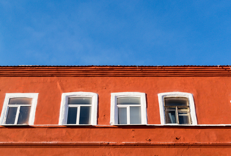 Bright orange painted aged building with four white windows set against a bright blue summer sky. Architectural image details with nobody and copy space.の写真素材
