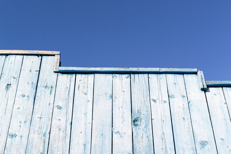 Old blue wooden wall and fence set against a blue sky background. Copy space area for designs and architecture themed ideas and text. Natural sunlight and worn wood pattern.の写真素材
