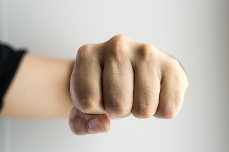 Close up image of a white male?s single clenched fist punching towards the viewer or frame. No rings or markings on the man?s hand. Copy space area for crime or fear based concepts and ideas. White backdrop.の写真素材
