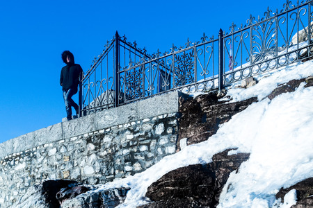 Young man standing on top of a surreal stone wall stares off thoughtfully into the unknown and...