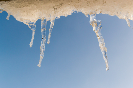 Winter sun melts icicles hanging from a roof top. Blue sky background with copy space area for holiday travel vacation text and designs.の写真素材