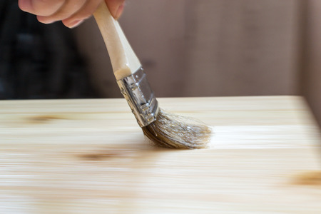 Female hand applies a varnish to a wooden surface. Intentional camera motion blur of the brush creates a sense of movement and activity in this home DIY image.の写真素材