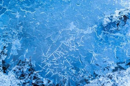 Blue ice texture of frozen water in a puddle with frozen crystal patterns and shapes.の写真素材