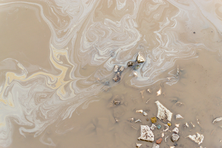 Weak Oil spill on the surface of a muddy grimy puddle of water.の写真素材
