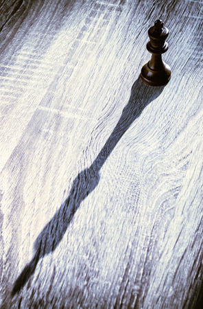 Single black king classical gaming chess piece on wooden background with elongated shadow.の写真素材