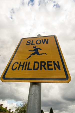 Yellow slow children warning sign with grey sky background. Copy space area for health and traffic safety designs.の写真素材