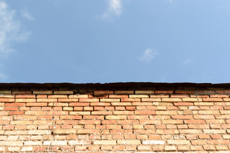 Old red stone brick wall with signs of wear set against a blue sky background. Copy space area for text.の写真素材