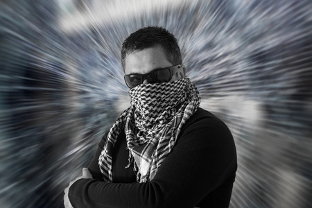 Mysterious single man wearing sunglasses and a keffiyeh with crossed arms with a defocused zooming...