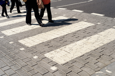 People walking across a white zebra crossing pedestrian road marking. Feet and legs with no faces and a copy space area.の写真素材