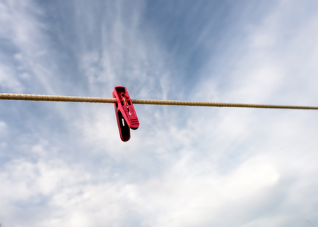 Single plastic red peg on a washing line set against a blue sky background with plentiful copy space area.の写真素材