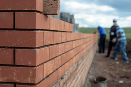 Newly built red brick wall of a newly built house with bricklayers in the backgroundの写真素材