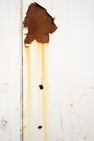Old rust spot and holes in orange with bleed runs on a white metal surface that has a grimy and grunge lookの写真素材