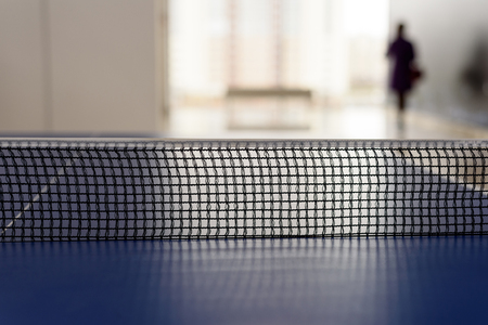 Black mesh tabletennis netting with a defocused background with a person walking away from the ping-pong tableの写真素材