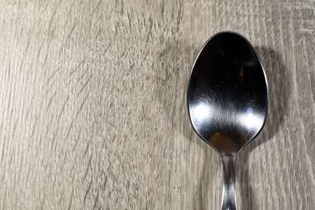 Single shiny empty silver spoon on a wooden kitchen background