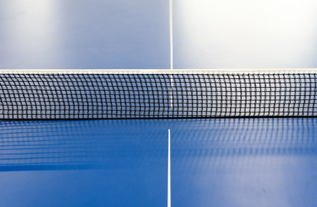 Horizontal table tennis net in black mesh dividing a blue colored table tennis. Copy space area for sports designs.の写真素材