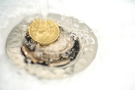 British money including a one pound coin stuck in a sink drain plughole as water flows over the...