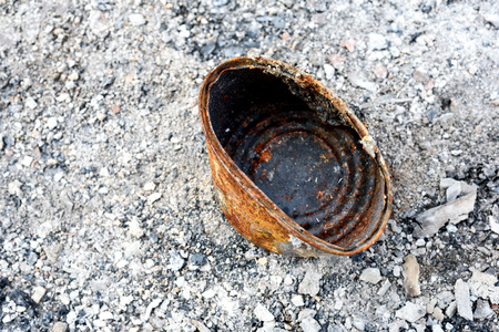 Burnt food can aged with rust sits in the ash remains of a fire
