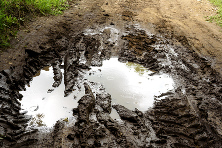 Rain filled muddy puddle with vehicle tracks on a dirt track roadの写真素材