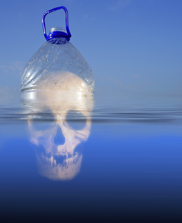 Pollution themed design of a plastic PET drinking container floating in sea water with a human skull submerged beneath the environmentの写真素材