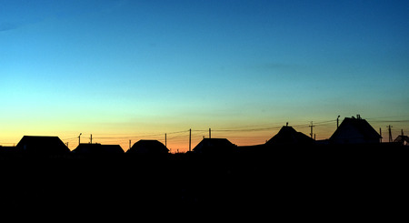 Roof lined village houses in silhouette against a dusk sky of fading blue lightの写真素材