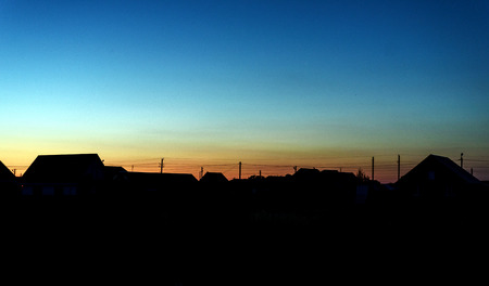 Roof lined village houses in silhouette against a dusk sky of fading blue lightの写真素材