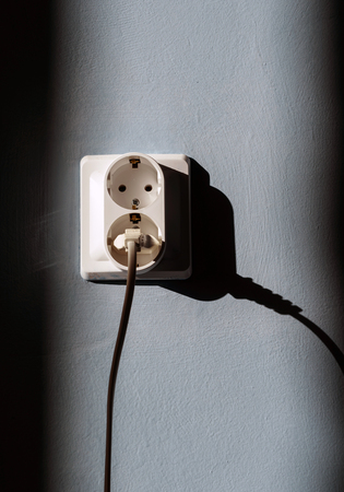 Electrical plug socket with electric cable inserted into one of the plugs with a blue wall background and sunlightの写真素材