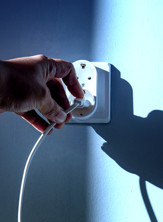 Man  hand pulls a plug from an electrical socket concept with a blue wall background and natural...